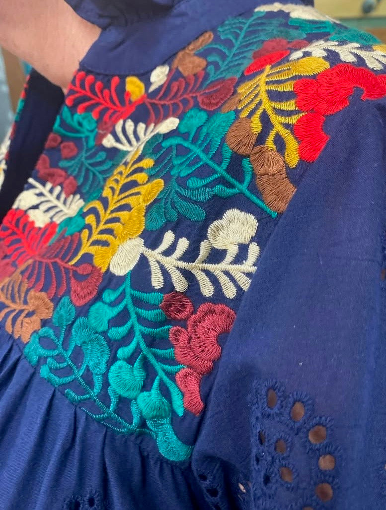 Close up of colorful embroidered neckline detail on navy eyelet cotton dress.