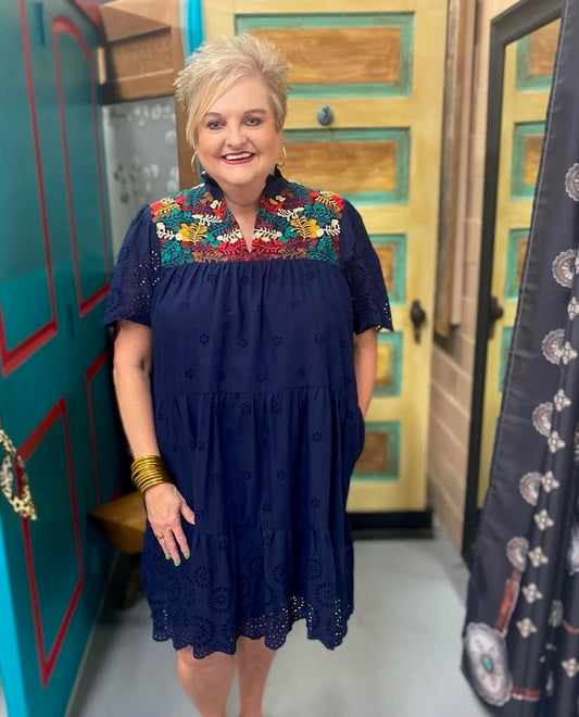 Woman wearing a navy cotton eyelet dress with embroidered neckline and pockets.