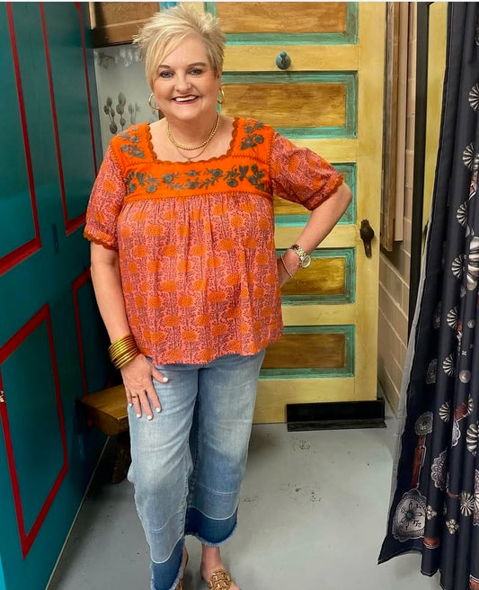 woman wearing an orange floral cotton Dia Top with embroidered details, paired with denim jeans