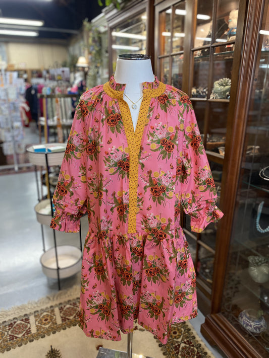 pink dress with bold floral print and yellow trim on a mannequin in boutique setting