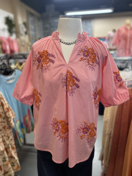 pink cotton top with orange and purple floral embroidery and ruffled neckline on mannequin